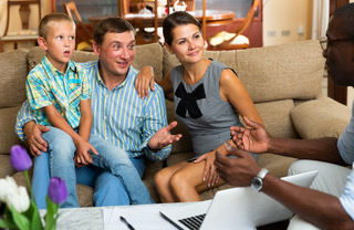 Familie mit Kind sitzt auf einer Couch und hört interessiert jemanden zu